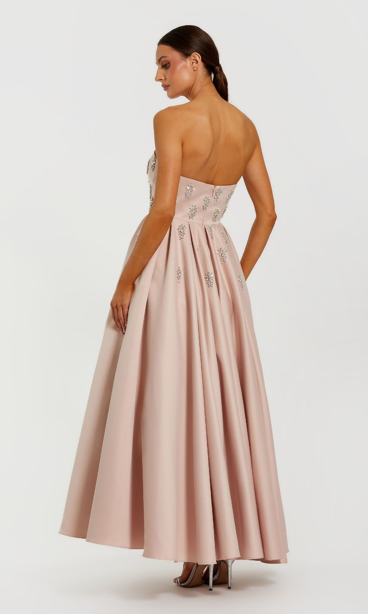 Woman wearing a pink evening gown with a backless design on a white background
